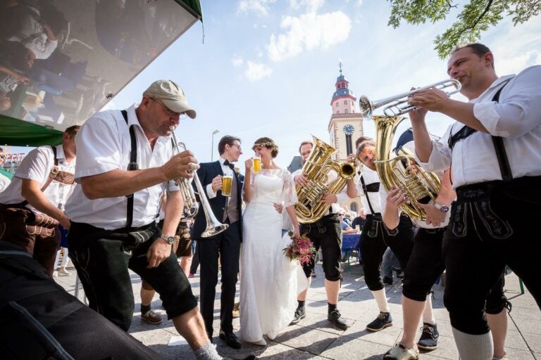 Das Brautpaar trinkt Bier mit einer Blaskapelle in der Kulisse der Innenstadt von Frankfurt am Main.